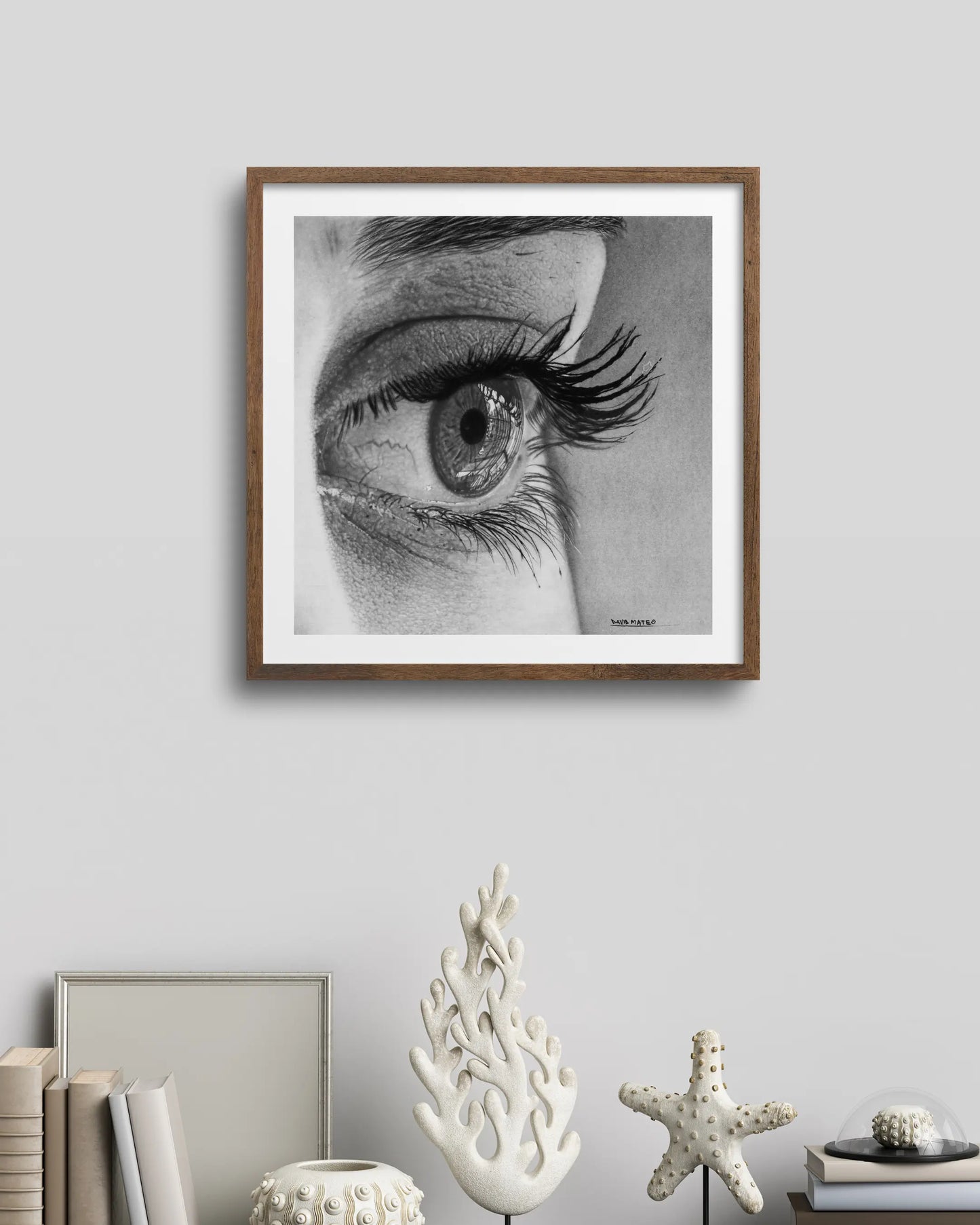 Lámina enmarcada y suspendida con cables. Presenta un dibujo a lápiz de un ojo humano de perfil con pestañas muy largas, destacando los reflejos en la córnea.