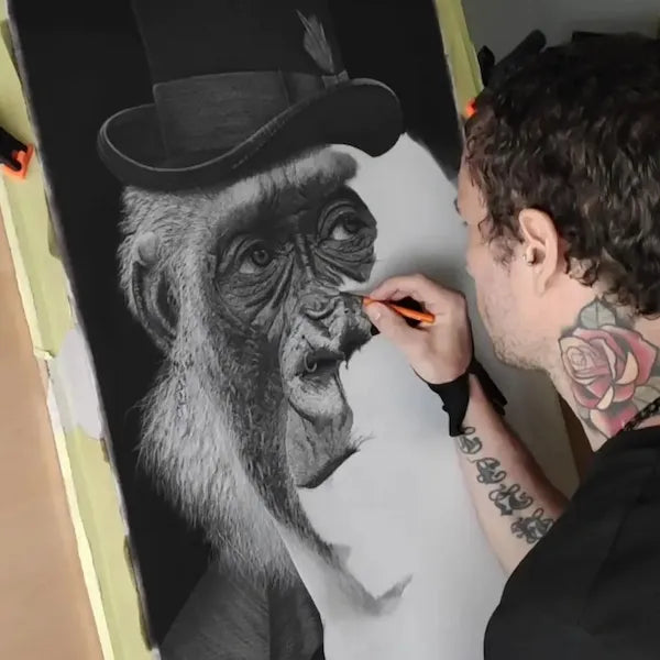 El artista David Mateo trabajando en un dibujo a lápiz en hiperrealismo a carboncillo de un gorila elegante con sombrero de copa. Muestra el proceso de creación y la técnica de alto contraste.