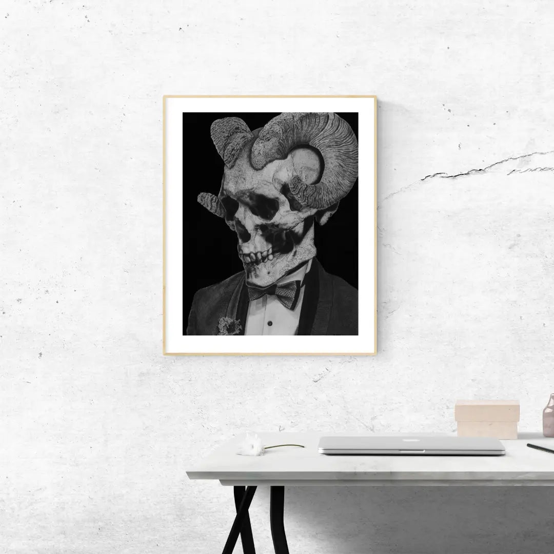 Lámina enmarcada en blanco sobre una estantería blanca. Muestra un dibujo monocromático de un cráneo con cuernos y vestido de traje, junto a un jarrón de planta.