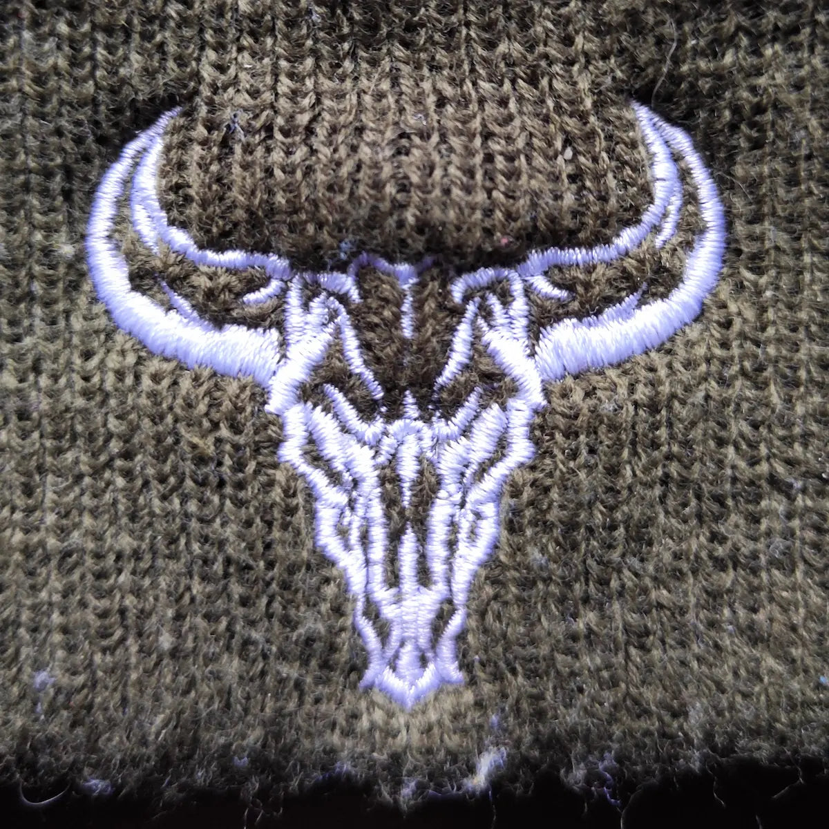 Primer plano del logo bordado blanco en un gorro de invierno del artista David Mateo Art.