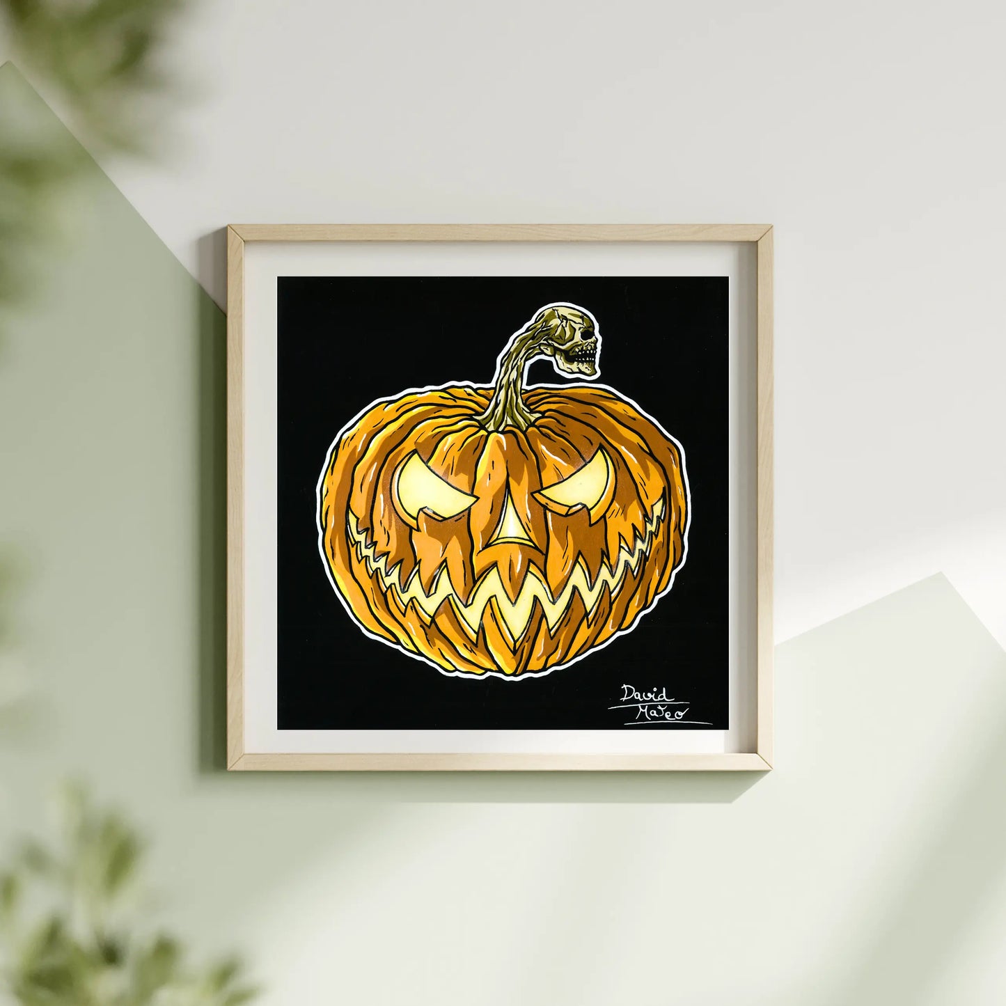 Lámina cuadrada enmarcada en madera, colgada en una pared blanca. Muestra un dibujo a color de una calabaza naranja con la cara iluminada sobre un fondo negro.