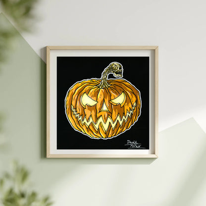 Lámina cuadrada enmarcada en madera, colgada en una pared blanca. Muestra un dibujo a color de una calabaza naranja con la cara iluminada sobre un fondo negro.