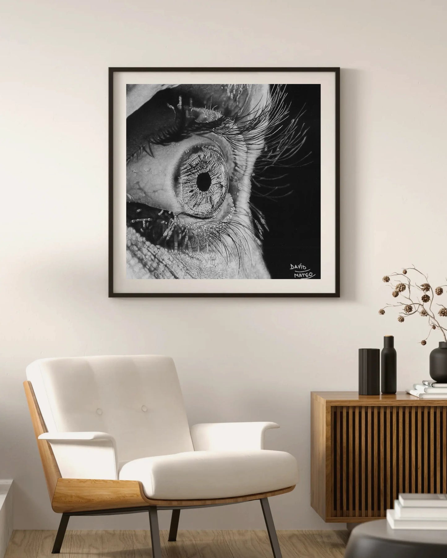 Lámina suspendida en un marco de madera clara. Presenta el dibujo a lápiz de un ojo humano muy abierto con la piel arrugada y pestañas largas.