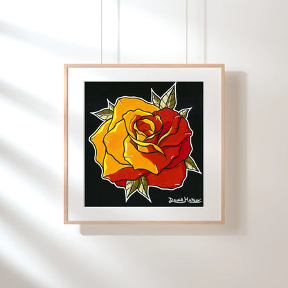 Lámina enmarcada en madera, sobre una pared verde pálido con sombras de luz solar. Muestra el dibujo a color de una rosa de pétalos rojos y amarillos, sobre fondo negro.